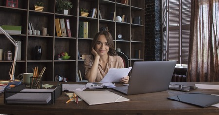Businesswoman sitting in chair at table and with smile holding in hand documentsの写真素材