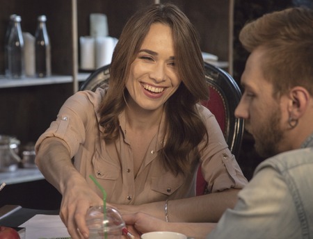 Young business woman laughing and giving cup with drink to young manの写真素材