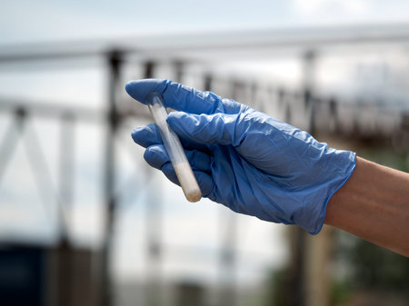 Hand in glove holding a test tube with a dry substance. Background sky, plant constructionの写真素材