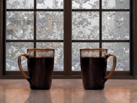 Two mugs with a hot drink - tea or coffee on the window sill of the window. Outside, winter, snow, snow patterns on glassの写真素材