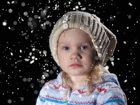 It's snowing. The baby in a cap. Snowfall. Face close. Amazing view of the little girl. Portrait. black Backgroundの写真素材