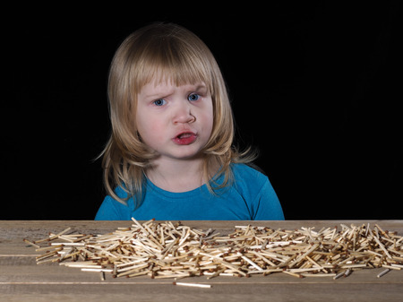 Little child and Lucifer match. Lucifer match are not toys for children. A lot of matches on the table. Child scared. Black background. Dangerous Games with fireの写真素材