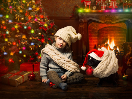 little sweet girl with a dog in a New Year's cap. Christmas tree, fireplace, festive interior roomの写真素材