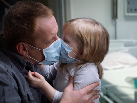 Hospital ward. Father kissing daughter through medical mask. Little daughter. Father hugs daughter. Concept - disease, infection, childhood diseases, virusesの写真素材