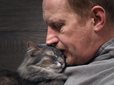 Man and cat - two profiles. Muzzle of a cat and a man's face. The man wrinkled. The cat and the owner smile. Cat gently pressed. Love cats and humans. Relationship, weasel. Background - a wooden boardの写真素材