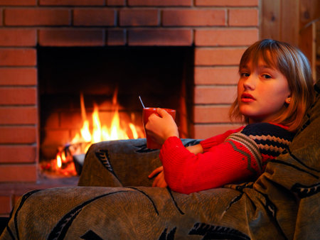 young girl with a mug of tea on the background of a burning fire in the fireplaceの写真素材