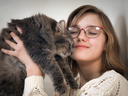 happy girl and a cat. Young girl in glasses and is holding a gray catの写真素材