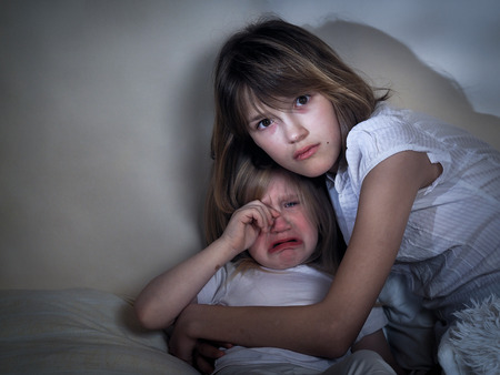 Sister teen hugs a crying little sister. Huge eyes, emotional eyes. Hatred, violence, punishment of childrenの写真素材