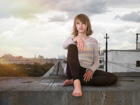Teenage girl sitting high on the roof. The city, the sun's raysの写真素材