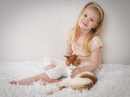 Happy little girl hugging a cat sitting on the bedの写真素材
