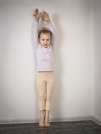 Little girl standing against the wall on tiptoe with raised arms. The child wants to grow upの写真素材