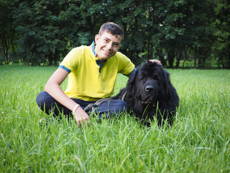 Laughing boy with a big dog. Green grass, Park. Dog breed Newfoundland