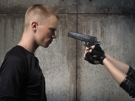 Young man. Female hand pointing the gun in the forehead the manの写真素材