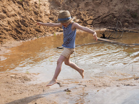 Happy child jumping in a large puddle. The summer heat, the child is barefoot