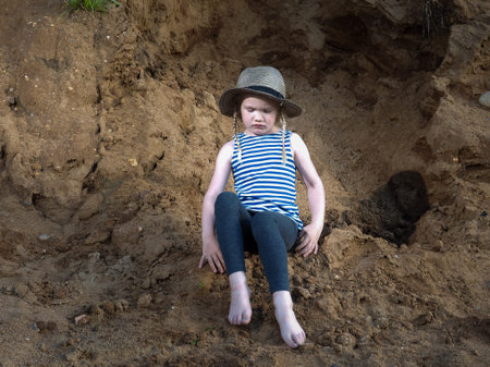 The child is sitting on the sand. The girl in the hat and barefootの写真素材