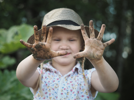 The child shows dirty hands. Girl covered in mudの写真素材