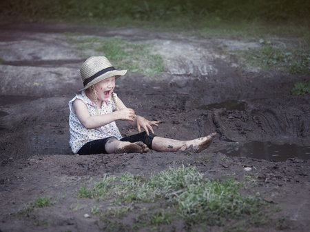 The child fell in a puddle. Dirty girl, crying. Rural road, mud