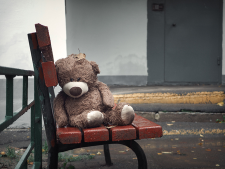 A toy bear is sad and wet on the bench at the entrance to the houseの写真素材