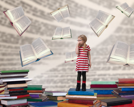 A small child with glasses standing among the books. The concept of education and reading. Preparation for schoolの写真素材