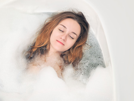 A young girl relaxes in the bath with foamの写真素材