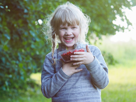 Baby with a bowl full of red currant berries. The girl laughs gleefully. Emotional portrait