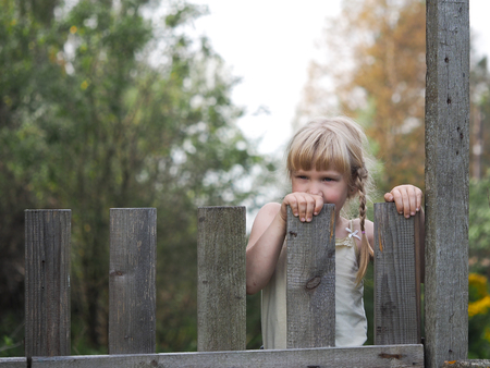 Girl looks through the old, wooden fence. Portrait of childの写真素材