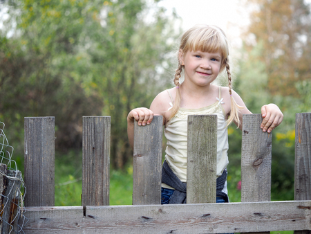 The child looks through the village fence. Portrait of funny little girlの写真素材