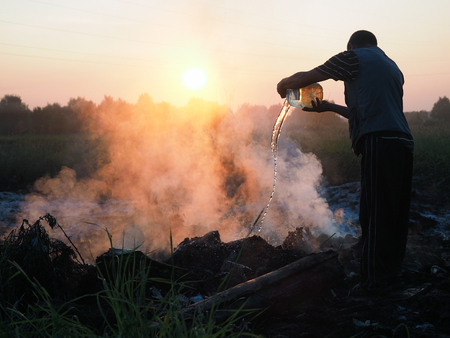 Fire in the field. Volunteers fighting the fire. Extinguish the flames with water from cans. The sunset, the silhouette of a man, smokeの写真素材