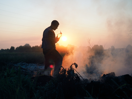 Fire in the field. Volunteers fighting the fire. Extinguish the flames with water from cans. The sunset, the silhouette of a man, smokeの写真素材