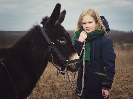 Donkey is the girl's favorite animal. A child with a donkey on a pastureの写真素材