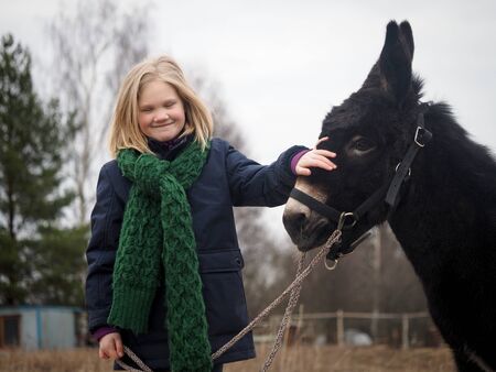 Donkey is the girl's favorite animal. A child with a donkey on a pastureの写真素材