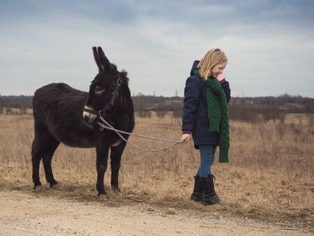 Donkey is the girl's favorite animal. A child with a donkey on a pastureの写真素材