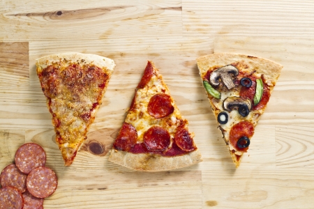 Top view of three baked pizza pie with slices of ham over wooden surfaceの写真素材