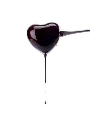 Close up image of a heart shaped pierced into fondue stick and coated with chocolate syrup against white backgroundの写真素材