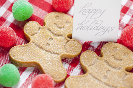 Close-up cropped image of gingerbread candies with happy holidays tag over red checked napkin 