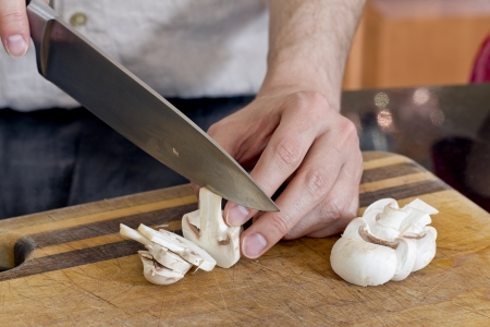 Close-up image of a human hand with knife slicing white mushroomの写真素材