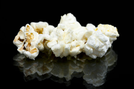 Pieces of white popcorn scattered over the glass table against the dark backgroundの写真素材