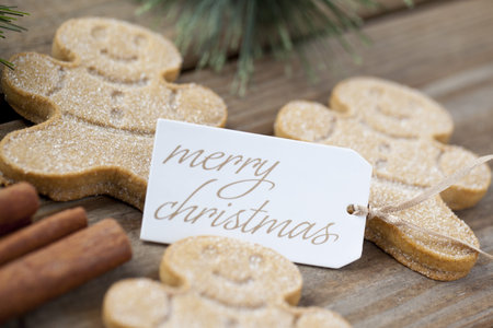 Close-up detailed view of merry Christmas tag with gingerbread candies over a wooden plank 