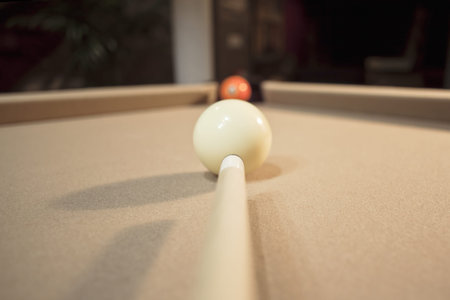 Close-up shot of pool stick and cue ball aiming at orange ball 
