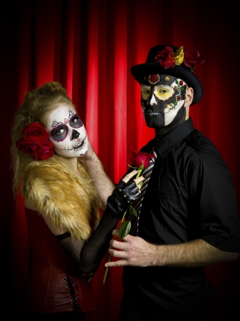 Portrait shot of ugly looking man with woman wearing sugar skull make up and holding rose over red background の写真素材