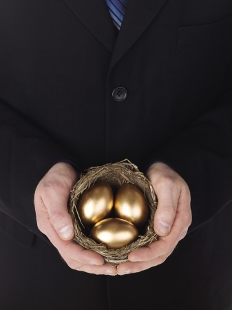 Close-up shot of a businessman holding golden eggs in nest. Model: Winter Bourneの写真素材