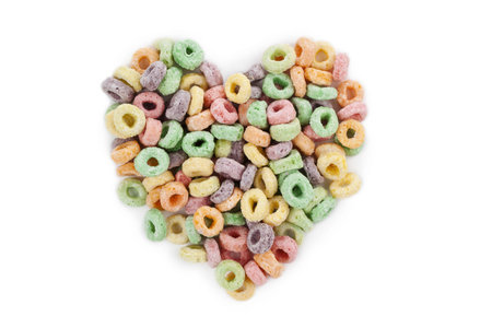 Overhead shot of colorful cereal arranged in heart shape on white surface.