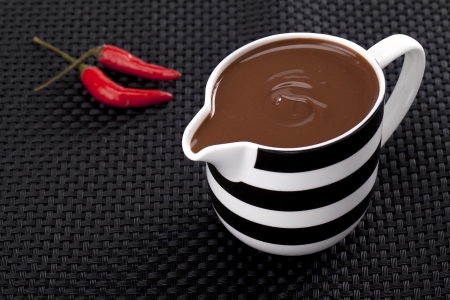 Close up image of red chili with cup of melted chocolate against black backgroundの写真素材