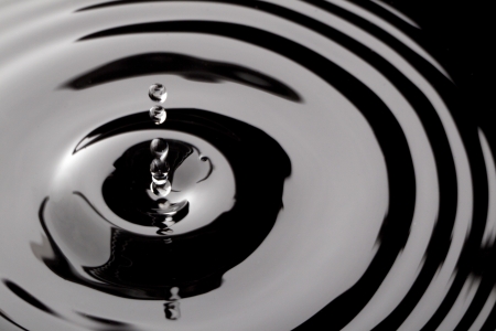 Water droplets falling on black water surfaceの写真素材