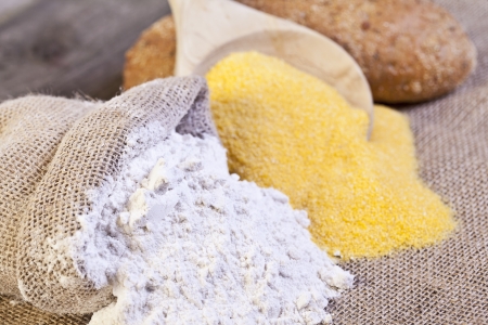 Spilled  burlap sack of wheat and maize flour with a wooden ladle and bread at the backgroundの写真素材