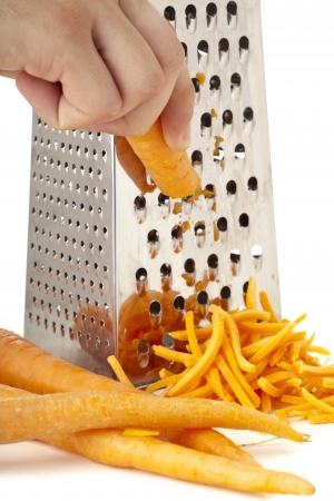Close-up image of human hand grating carrots over the white backgroundの写真素材