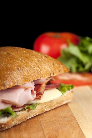 Close-up image of a bacon sandwich on a wooden table with a blurred tomato on the backgroundの写真素材