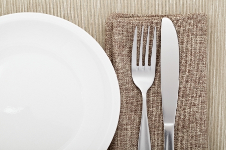 Image of a white plate with metallic knife and fork on the wooden tableの写真素材