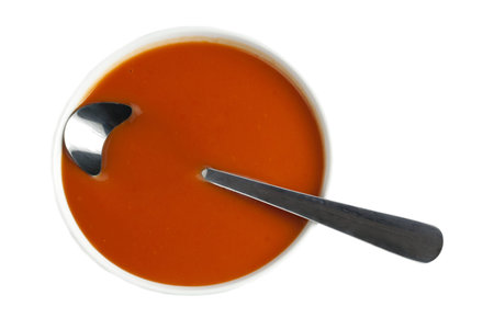 Top view image of a tomato soup bowl with spoon against white backgroundの写真素材