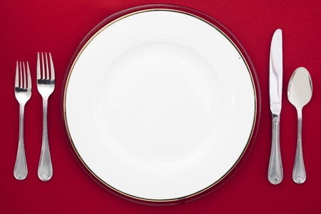 Image of a white round plate with knife, spoon and fork over the dinner tableの写真素材